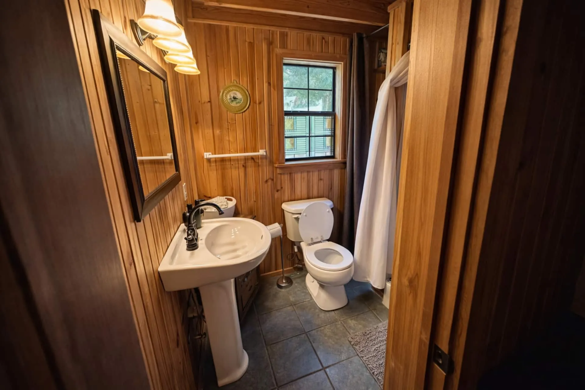 Cabin bathroom with a pedestal sink, framed mirror, sconce lighting and slate tile floor