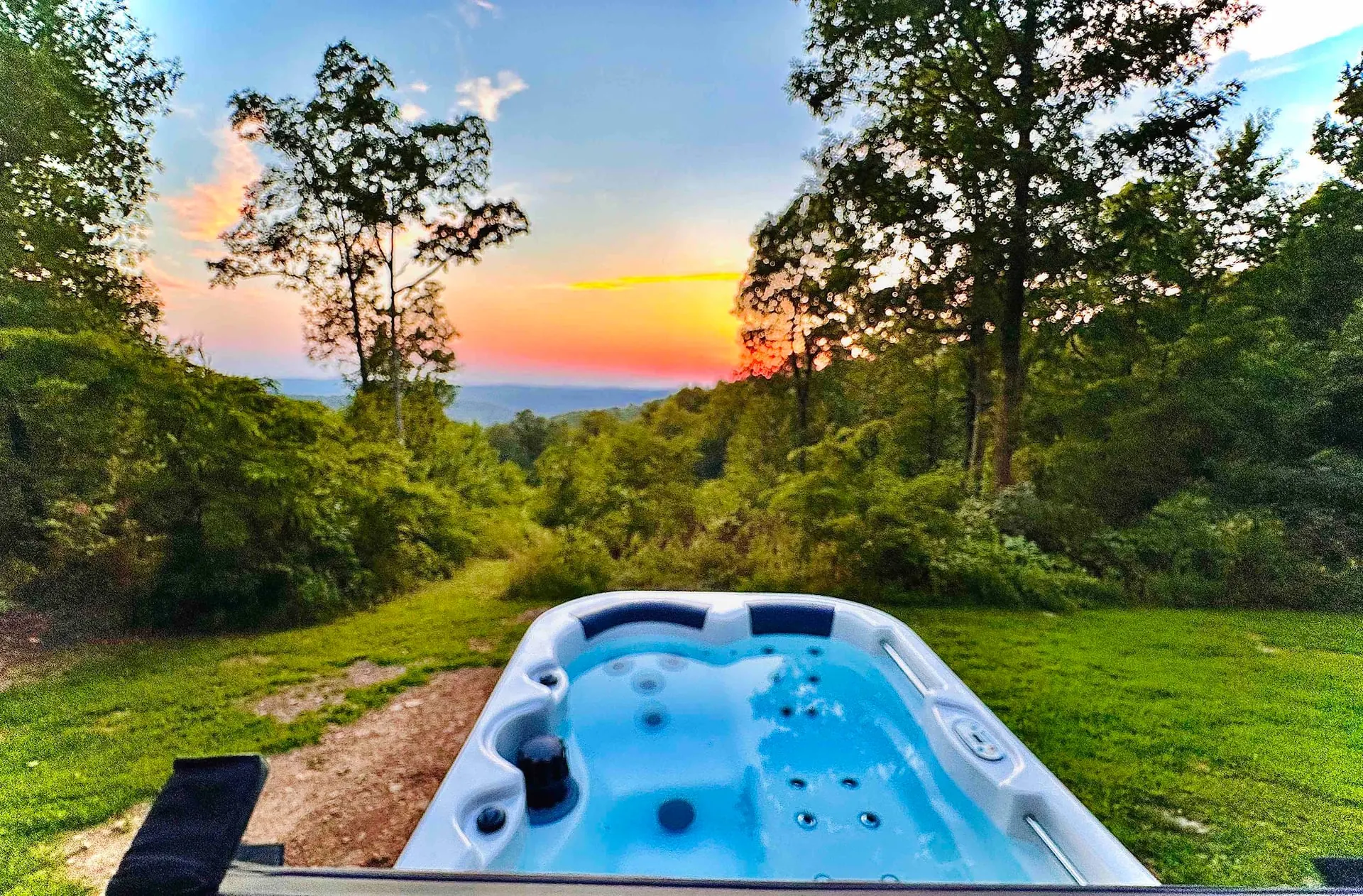 Private hot tub on the lawn at sunset, steam rising, overlooking the Buffalo River valley under a pink and orange Ozark sky