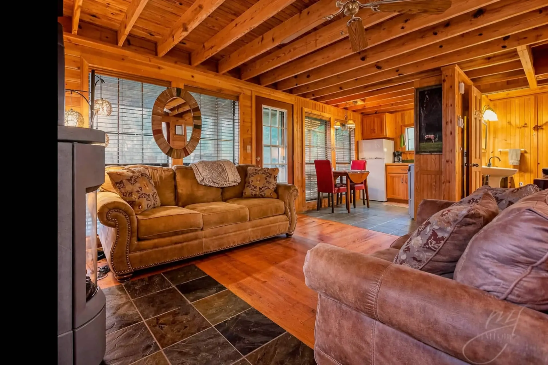 Open-plan living area looking through to the kitchen and dining table, with log walls and a pine-clad ceiling