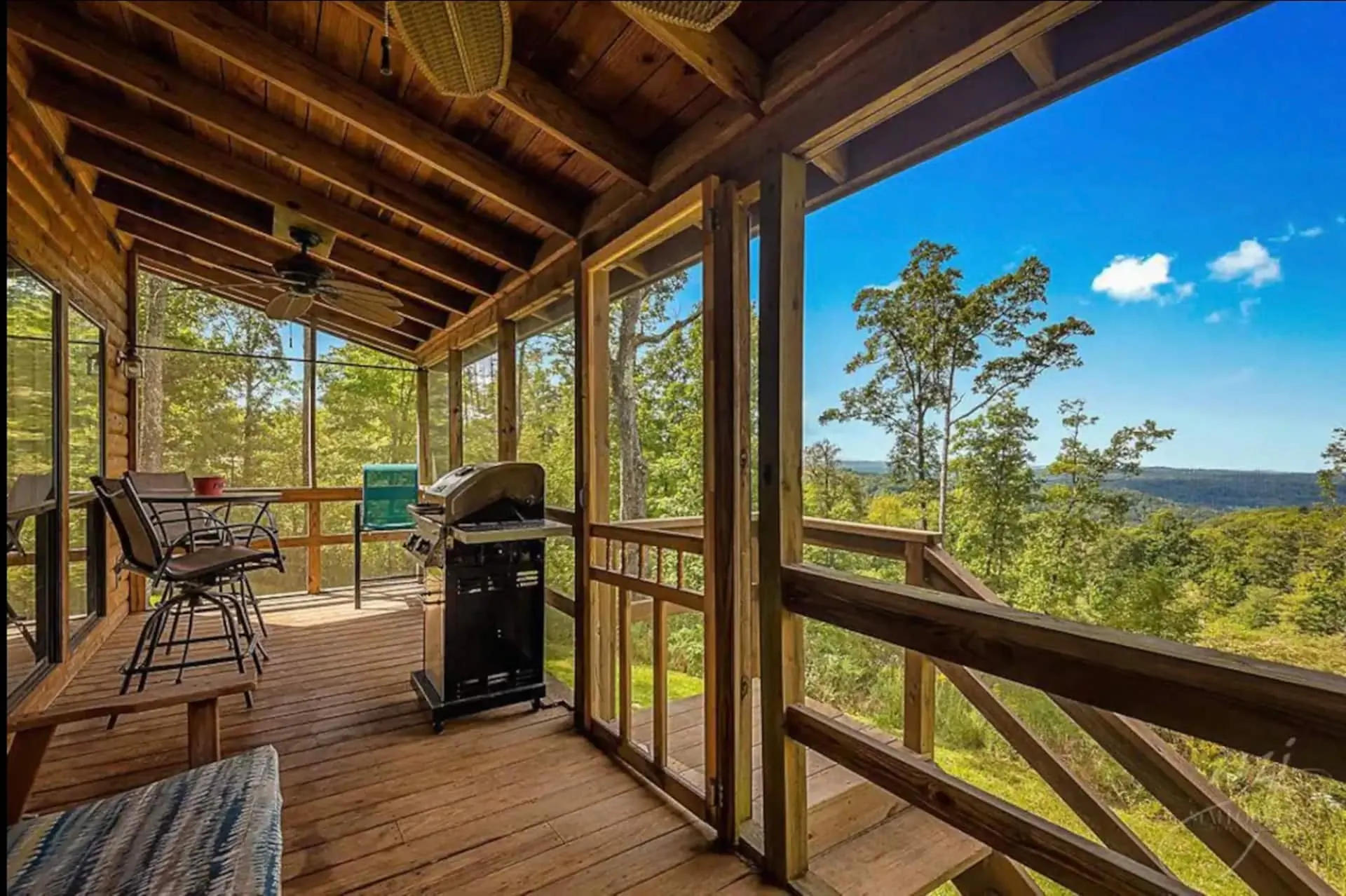 Screened back porch with a gas grill and bistro table, looking out over treetops to the layered Ozark ridgelines